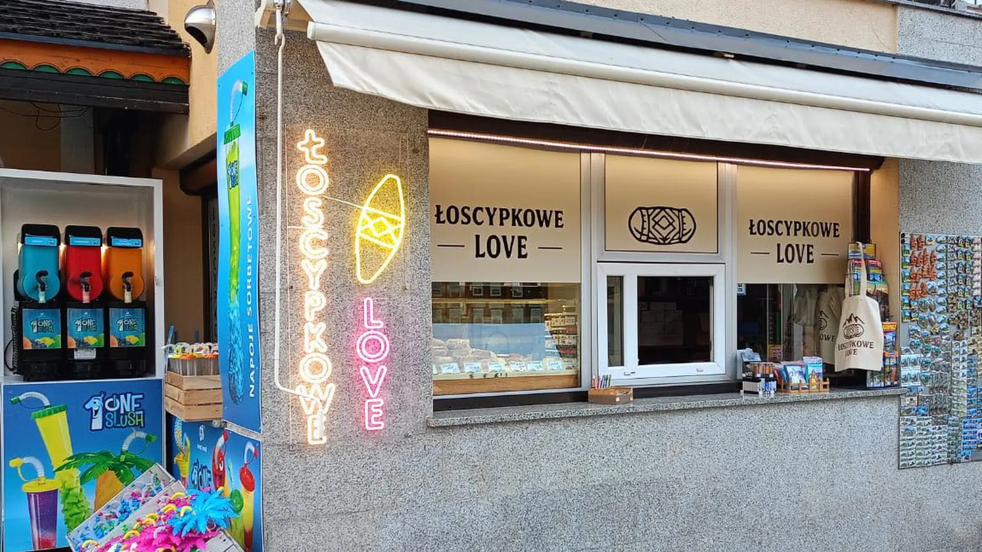Okienko sklepu Łoscypkowe Love wieczorem na deptaku w Karpaczu: neon na rogu, witryna z serkami